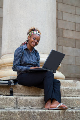 African American college student with laptop on library steps